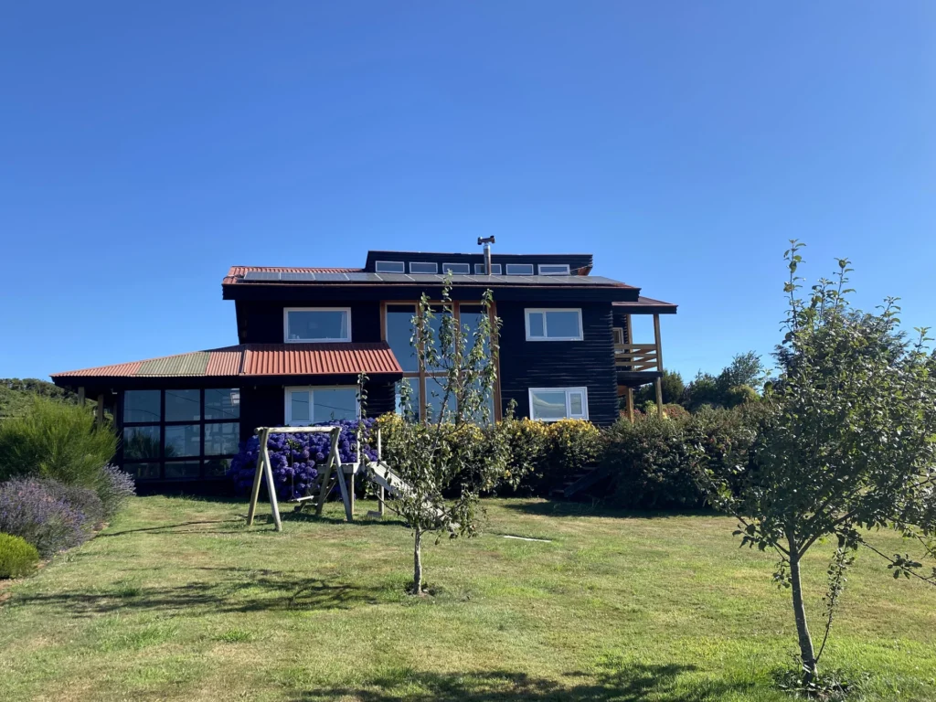 Casa KA vista desde el jardín, con cubierta roja y espacio vidriado.