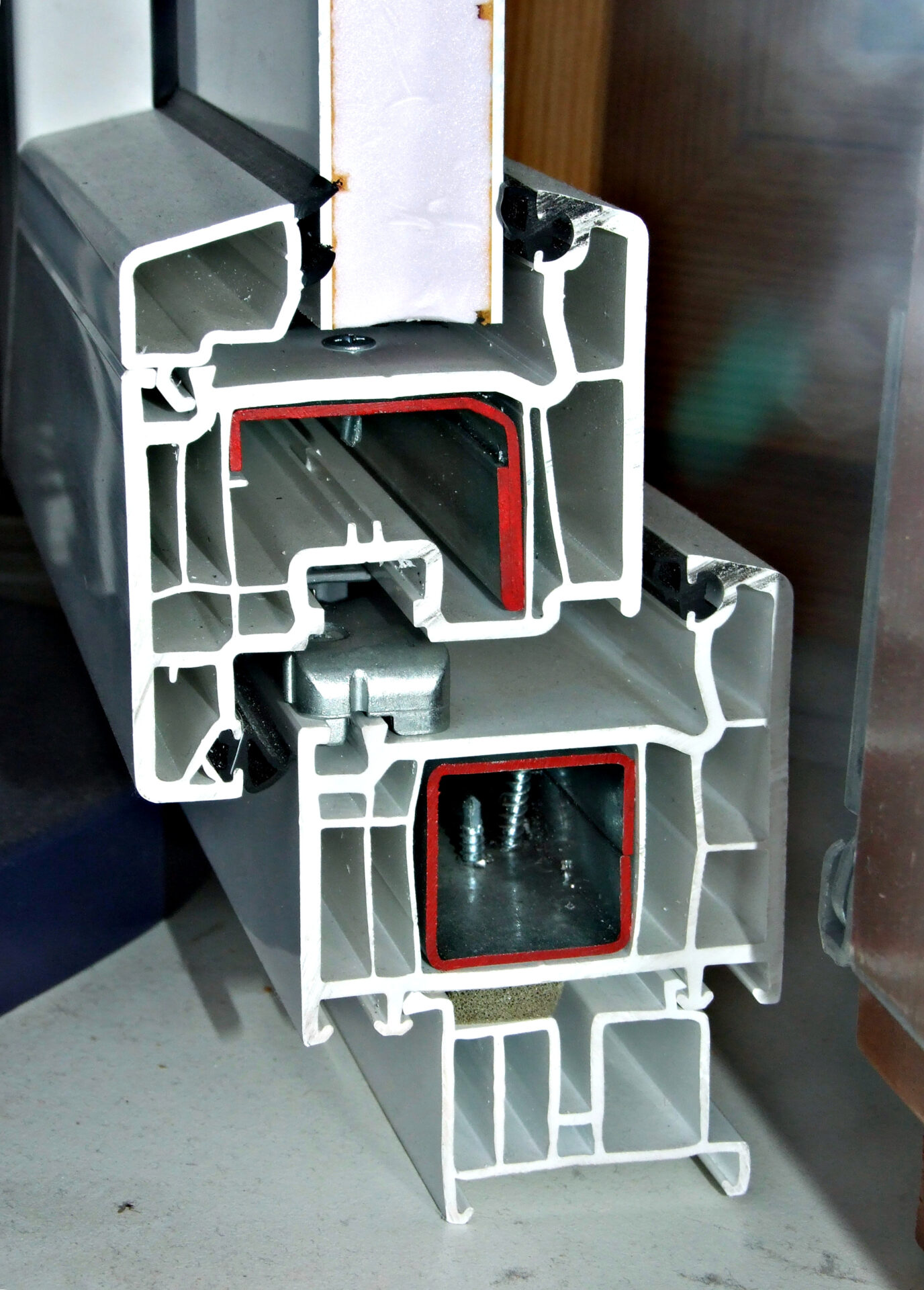 Corte de un perfil blanco de ventana de PVC con cámaras interiores, refuerzos metálicos y sellos.